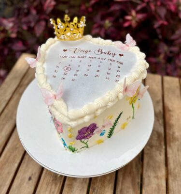 Burncake en forma de corazón, decorado con flores en buttercream en tonos delicados y una corona de bisutería brillante que le da un toque elegante y especial.