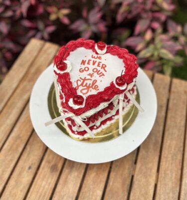 Burncake bañado en buttercream, decorado con perlitas, lazos de tela y cerezas en la parte superior.