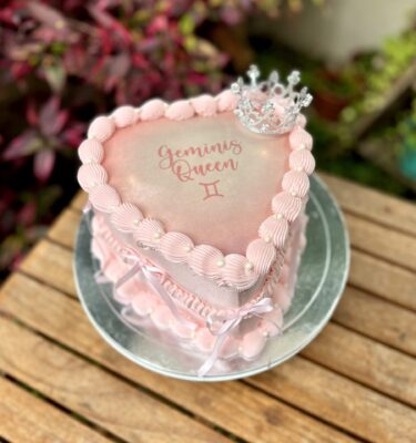 Burncake bañado en buttercream, decorado con lazos de tela a los lados, una pequeña corona de bisutería en la parte superior y perlitas brillantes.