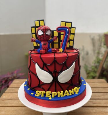 Torta de un piso temática de Spiderman con acabado en fondant, figura 3D de Spiderman en la cima y edificios en fondant.