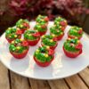 Mini cupcakes decorados con buttercream verde en forma de corona navideña, con perlitas comestibles y un lazo de fondant rojo.