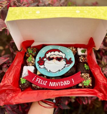 Caja navideña con 20 postrecitos surtidos —trufas, alfajores y brownies— decorada con detalles de Santa Claus en fondant y la frase “Feliz Navidad”