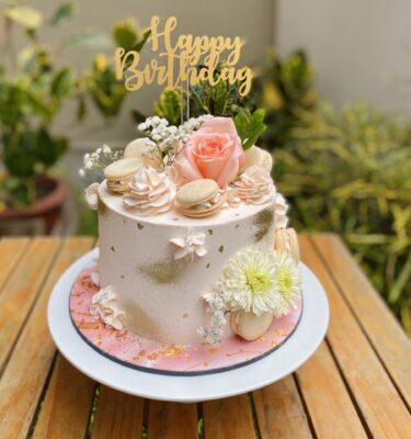 Torta bañada en buttercream suave, decorada con macarons y flores naturales en tonos delicados.