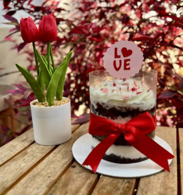 Bloom Cake: torta naked con buttercream, sprinkles temáticos de San Valentín, lazo decorativo, pequeño topper y macetero con flores artificiales.