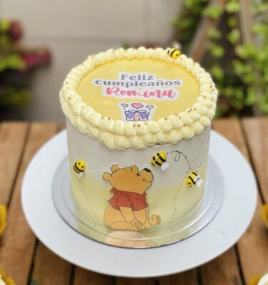 Burncake temática de Winnie Pooh decorada con abejitas de fondant y una imagen de Winnie Pooh en papel de arroz en el centro de la torta.