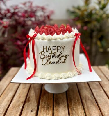 Torta bañada en buttercream, decorada con frambuesas frescas en la parte superior, lazos de tela en los laterales y un topper decorativo al frente.